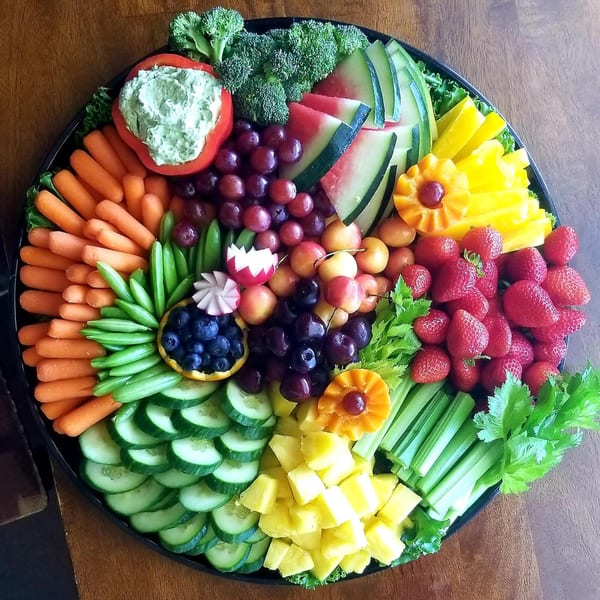 A large deli platter filled with fresh fruits and vegetables, including dip in a red bell pepper.