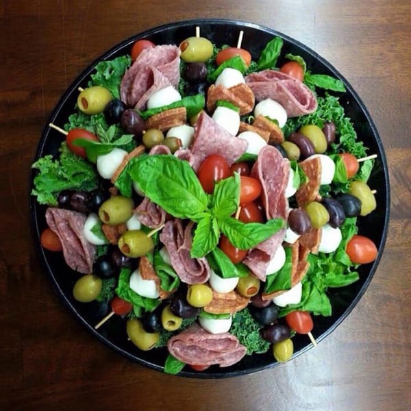 A deli platter with salami, mozzarella, olives, tomatoes, and basil on a bed of lettuce.
