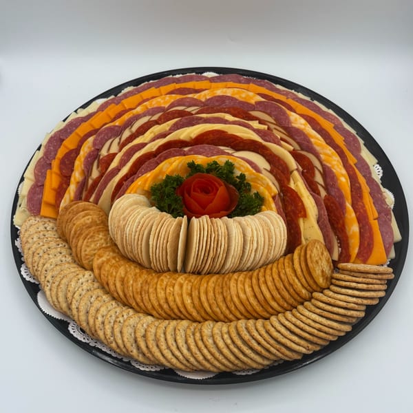 A deli platter with rows of sliced meats, cheeses, and crackers, garnished with a tomato rose.