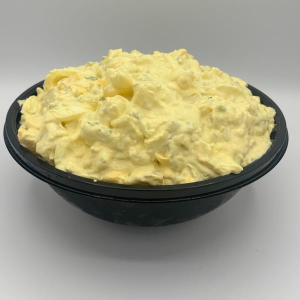 A large black bowl filled with creamy yellow potato salad, against a white background.