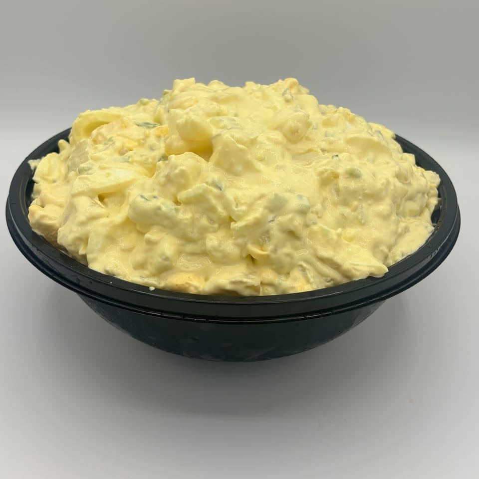 A large black bowl filled with creamy yellow potato salad, against a white background.