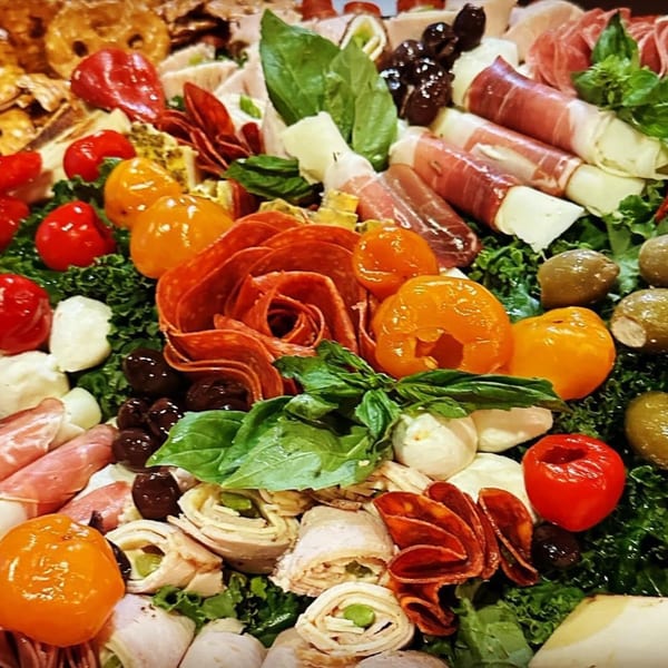 A vibrant Harvest deli platter with meats, cheeses, olives, peppers, and fresh basil.