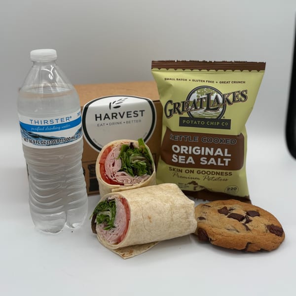 A Harvest deli lunch box with a turkey wrap, chips, chocolate chip cookie, and bottled water.