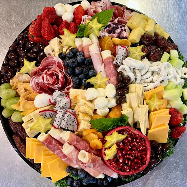 A large Harvest deli charcuterie board overflowing with cheeses, meats, fruits, and snacks.