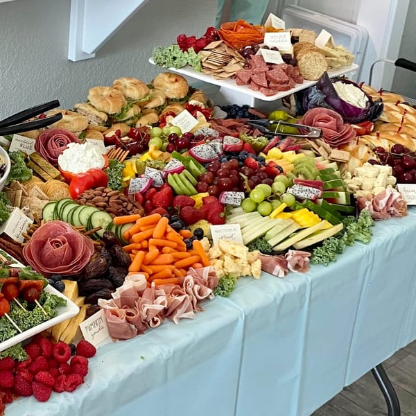 A large Harvest deli charcuterie board overflows with meats, cheeses, fruits, vegetables, and sandwiches.