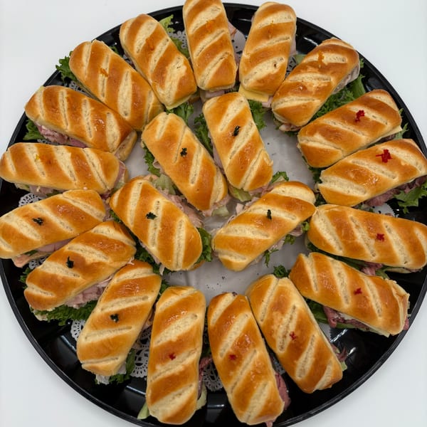 A black platter filled with Harvest deli's mini baguette sandwiches, featuring various fillings and toothpicks.