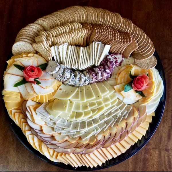 A large deli platter with various cheeses, crackers, and two decorative meat roses.