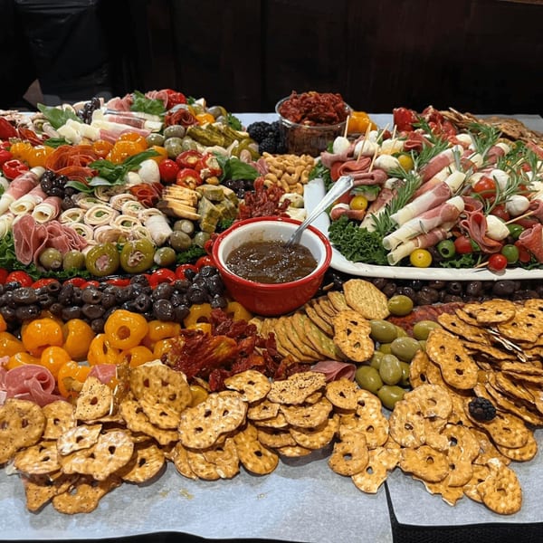 A large Harvest deli charcuterie board overflowing with meats, cheeses, olives, crackers, and fruit.