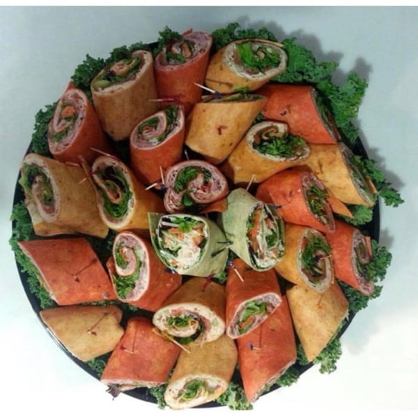 A catering platter of Harvest deli wraps in various colors, garnished with kale.