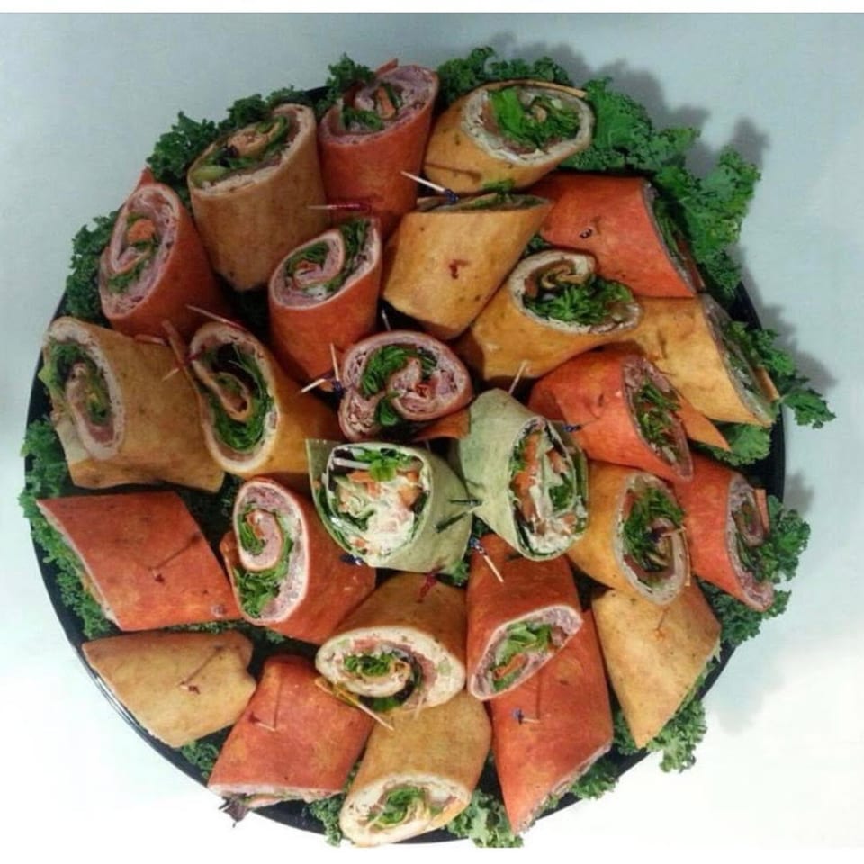 A catering platter of Harvest deli wraps in various colors, garnished with kale.