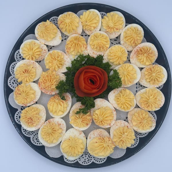 A platter of deviled eggs with paprika, garnished with parsley and a tomato rose.